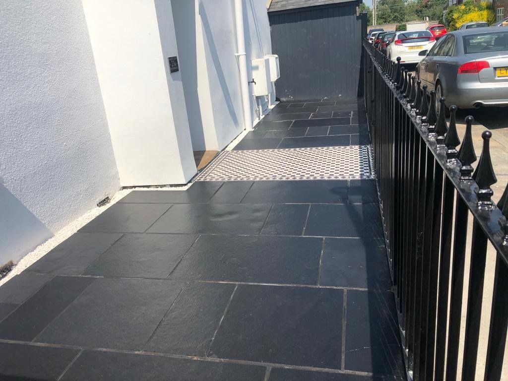 A black tiled walkway next to a fence with cars parked behind it