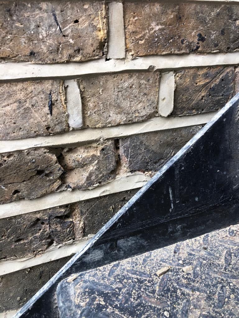 A close up of a brick wall with a black bucket in front of it.