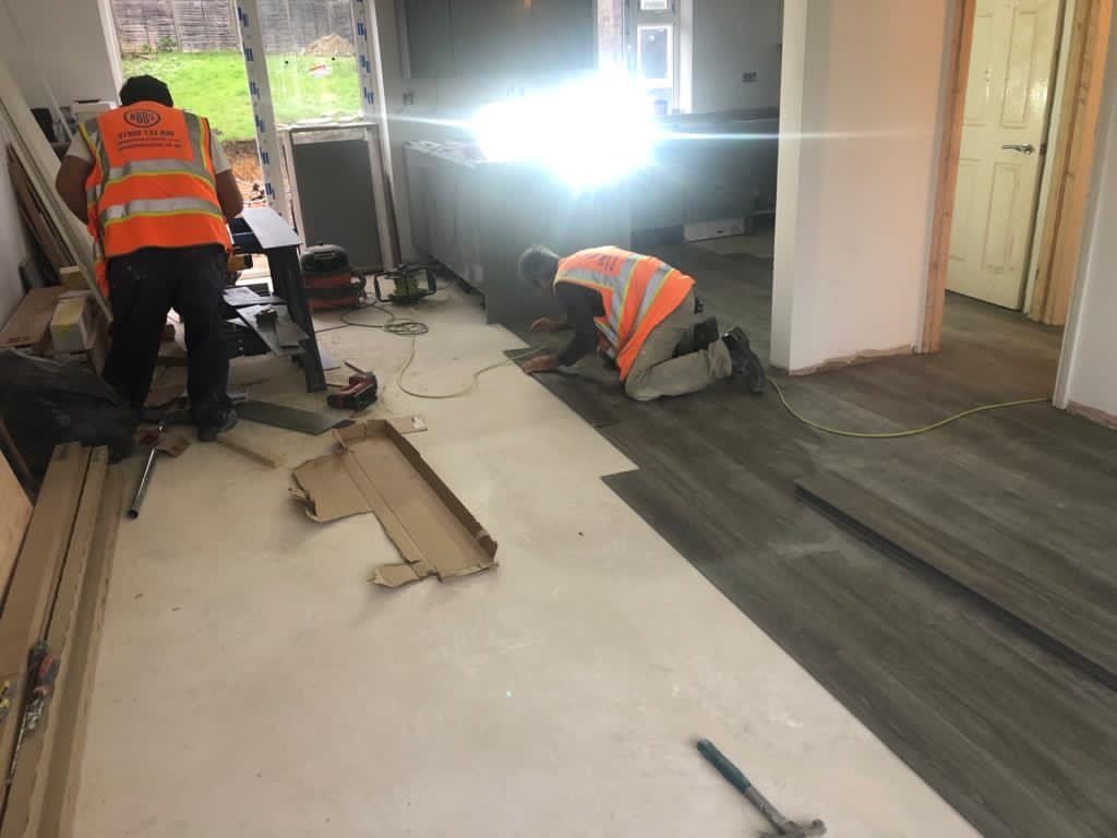 Two men are installing a wooden floor in a room.