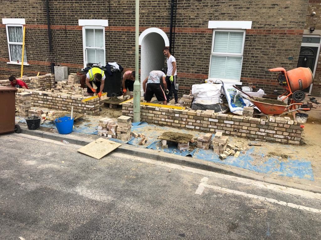 A group of people are working on a brick wall in front of a brick building.