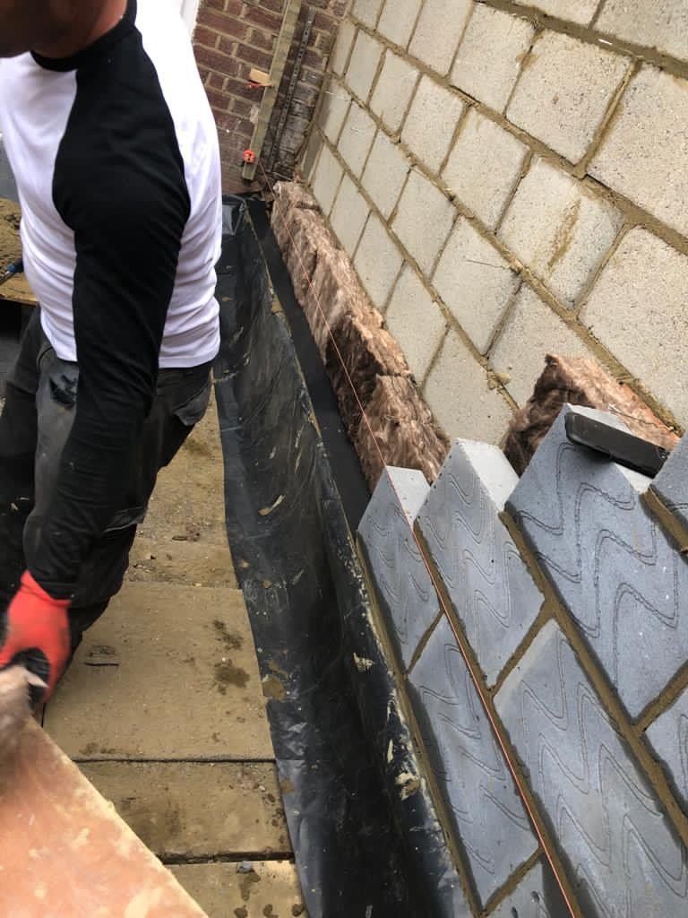 A man wearing red gloves is working on a brick wall.