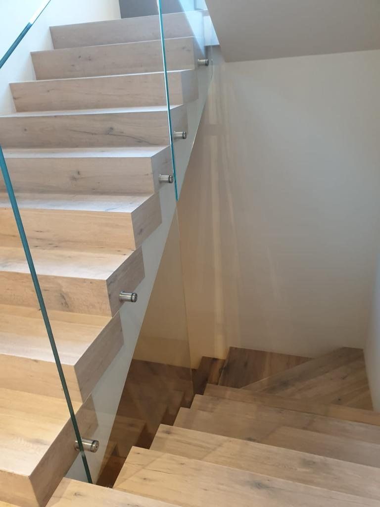 A set of wooden stairs with a glass railing.