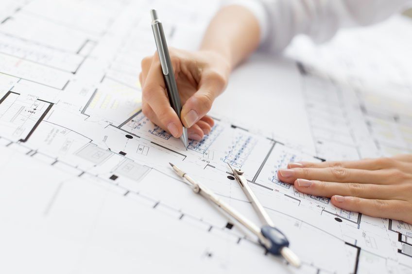 A person is writing on a blueprint with a pen and compass.