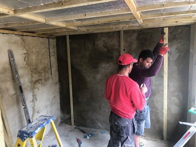 Two men are working on a wall in a room.