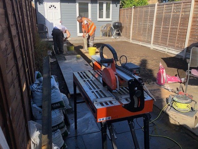 A man is using a circular saw to cut tiles in a backyard.