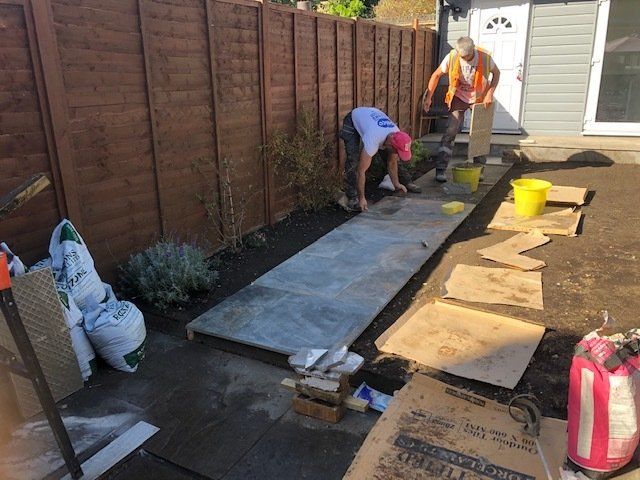 Two men are working on a concrete walkway in a backyard.