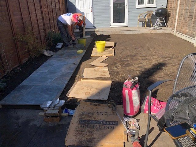 A man is working on a sidewalk in a backyard.
