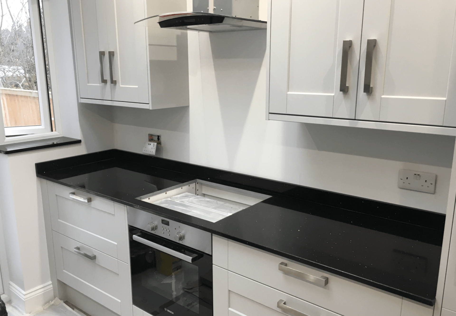 A kitchen with white cabinets and black counter tops.