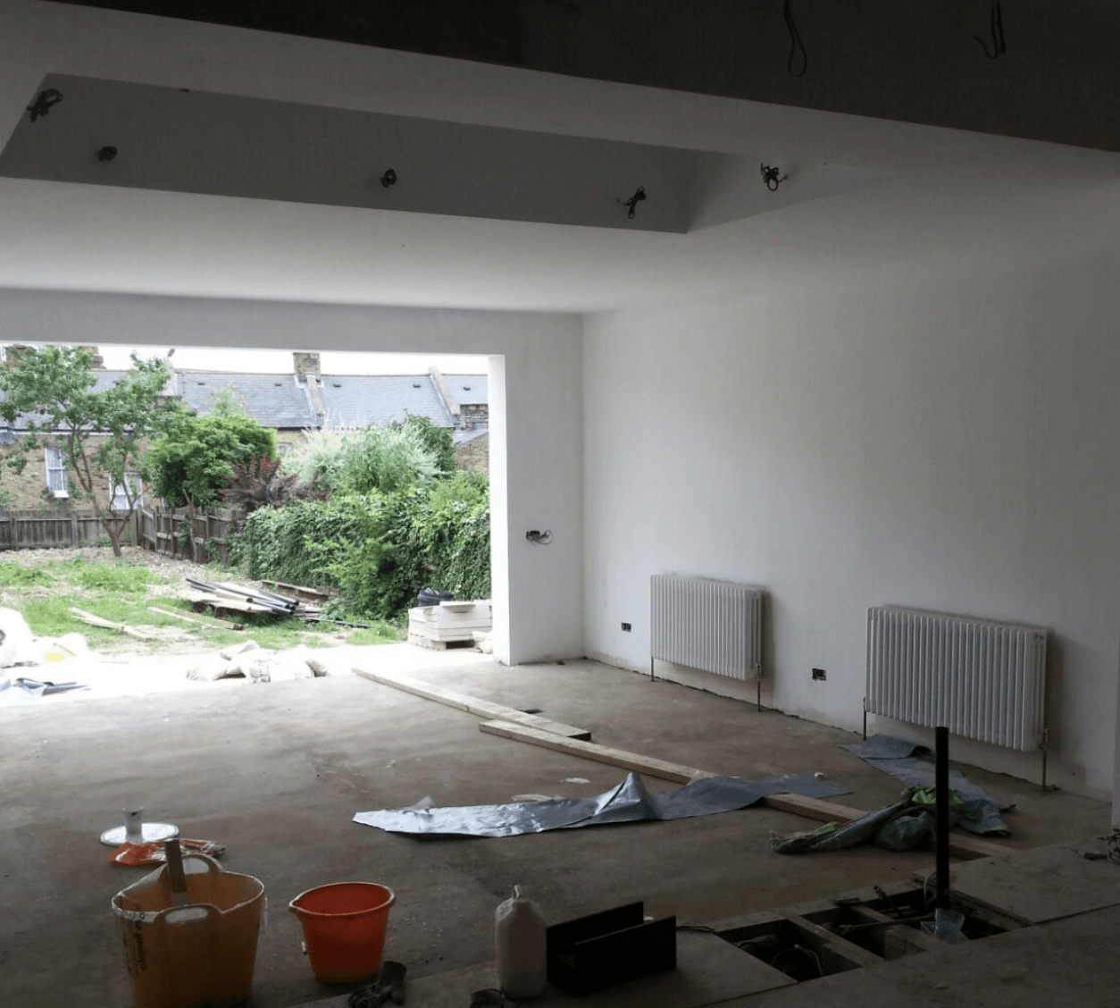 An empty room with buckets and a radiator on the floor