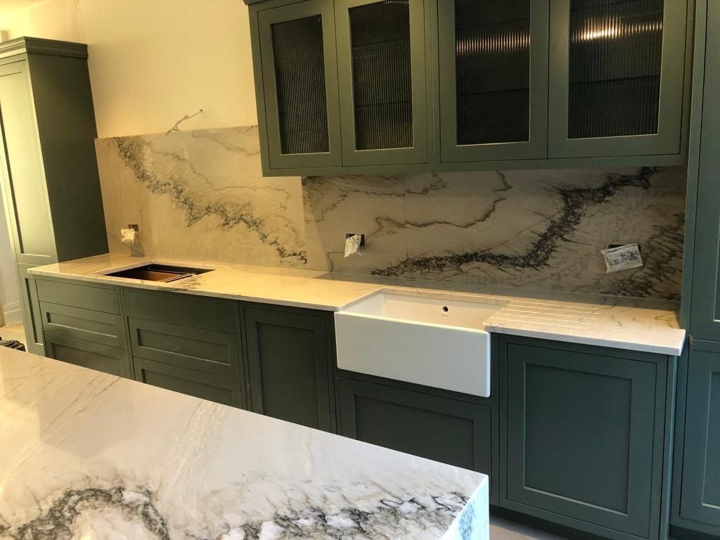 A kitchen with green cabinets , white counter tops , and a white sink.