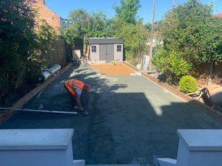 A man is working on a driveway in a backyard.