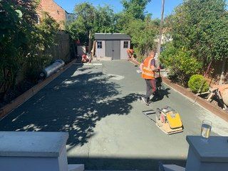 A man is working on a driveway in a backyard.