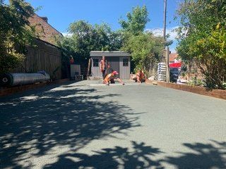 A group of people are working on a driveway in a backyard.