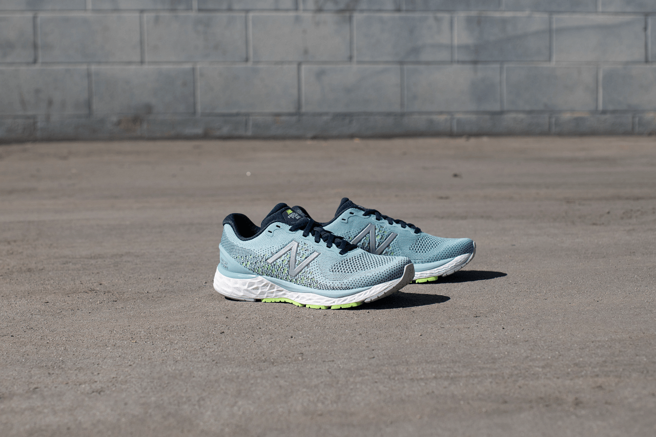 A pair of running shoes are sitting on the ground in front of a brick wall.