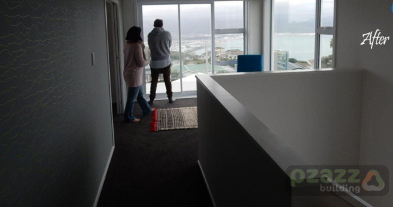 A man and a woman are standing in a 2 story house looking out a window.