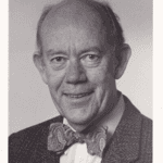 A black and white photo of a man in a suit and bow tie.