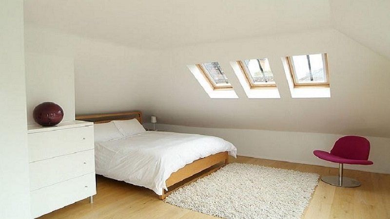 A bedroom with a bed , dresser , chair and skylights.