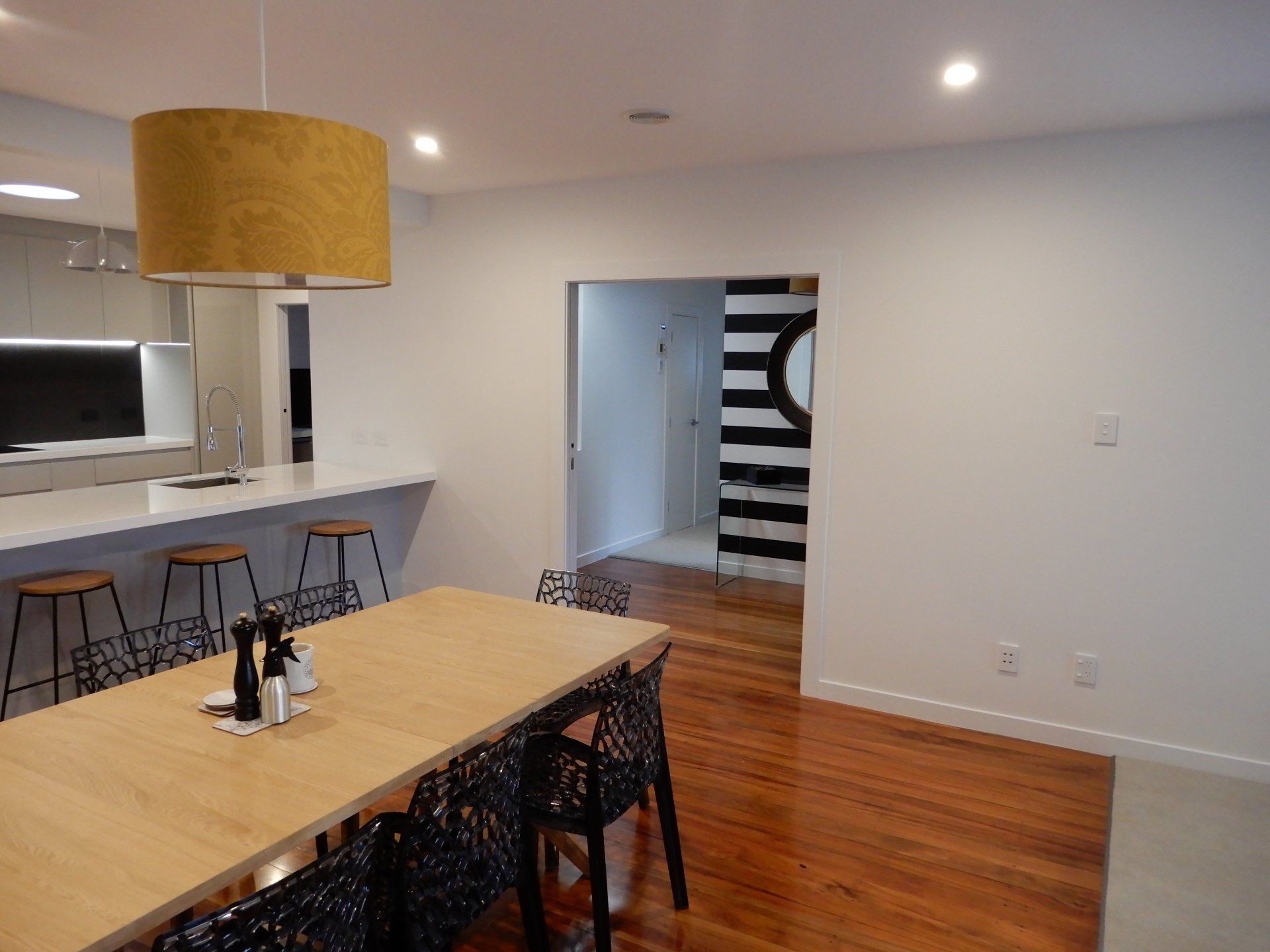 A dining room with a wooden table and chairs and a yellow lamp hanging from the ceiling.