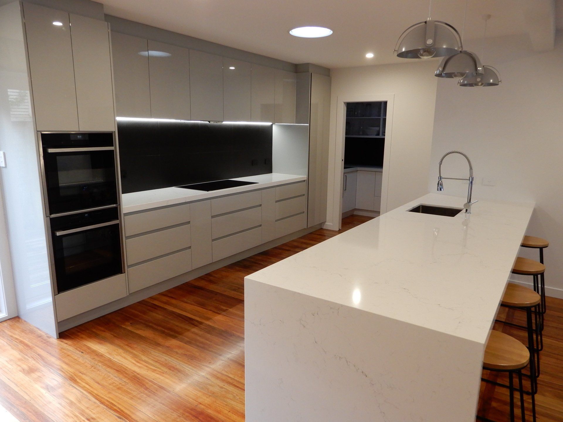 A kitchen with white cabinets , a large island , a sink , and stools.