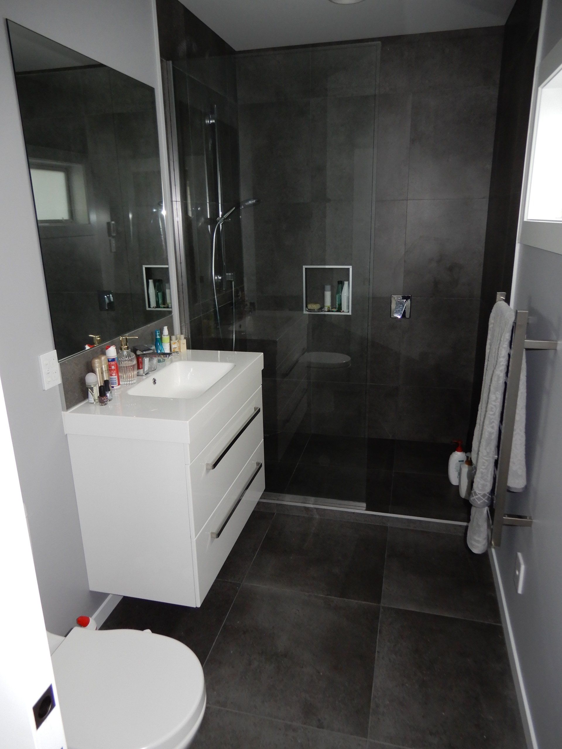 A bathroom with a toilet , sink , mirror and walk in shower.