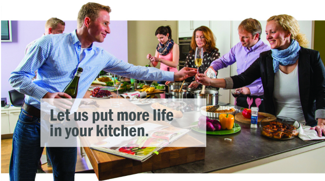 A group of people are standing around a table in a kitchen.