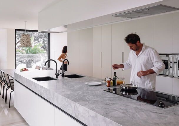 A man is cooking in a kitchen with a woman standing in the background