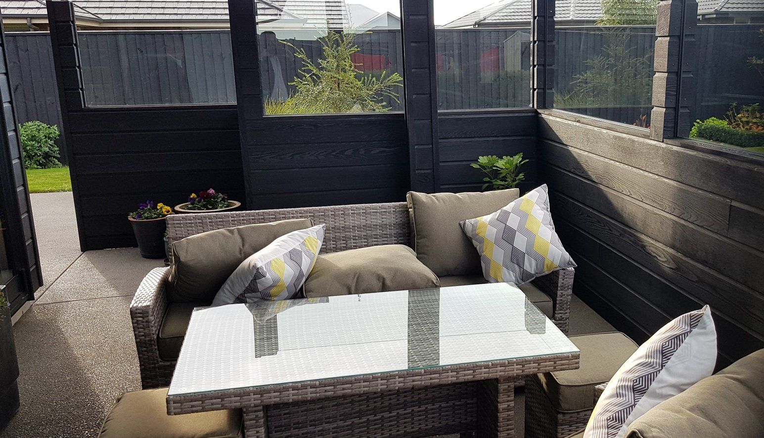 A patio with a couch , table , chairs and pillows.