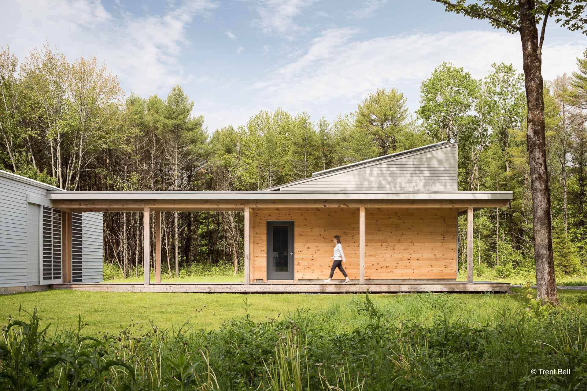 A man is walking in front of a wooden house with a porch.