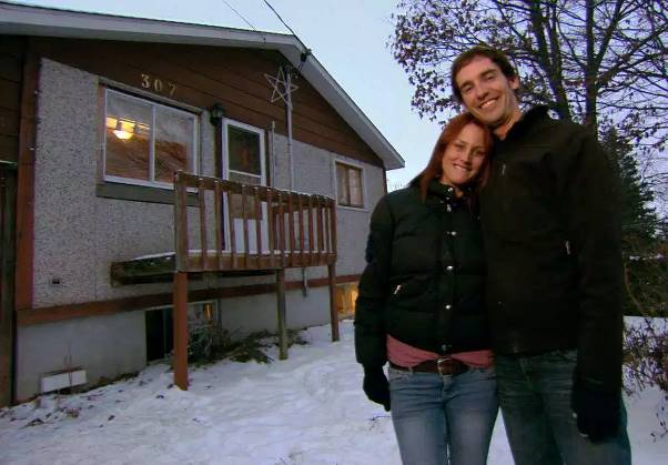 A man and a woman are standing in front of a house with the number 387 on it