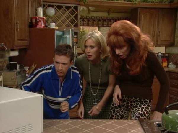 A man and two women are looking at a microwave in a kitchen