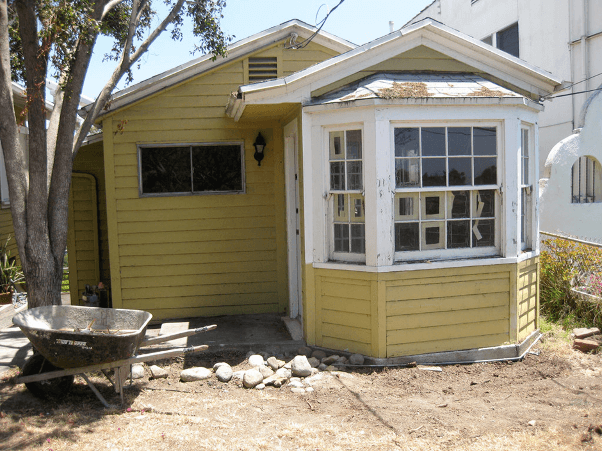 A yellow house with a wheelbarrow in front of it