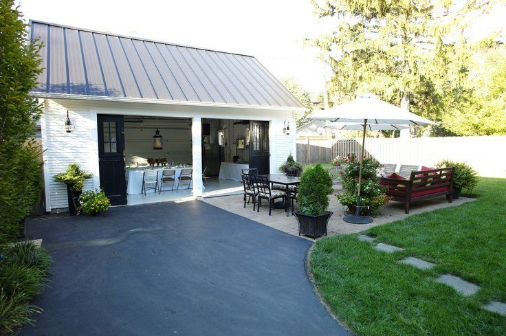 A white garage with a brown roof is open to a patio area.
