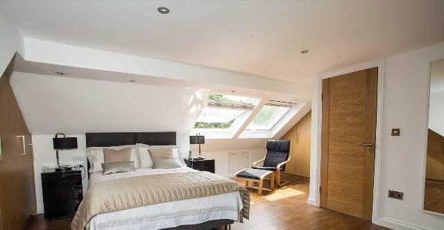 A bedroom with a bed , chair , mirror and skylights.