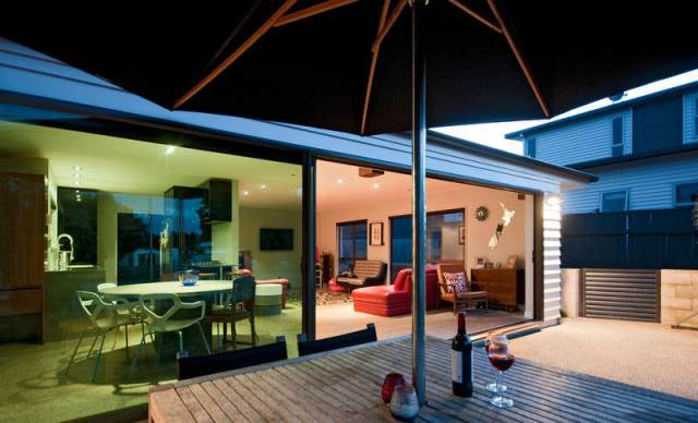 A table with a bottle of wine and glasses under an umbrella in front of a house.