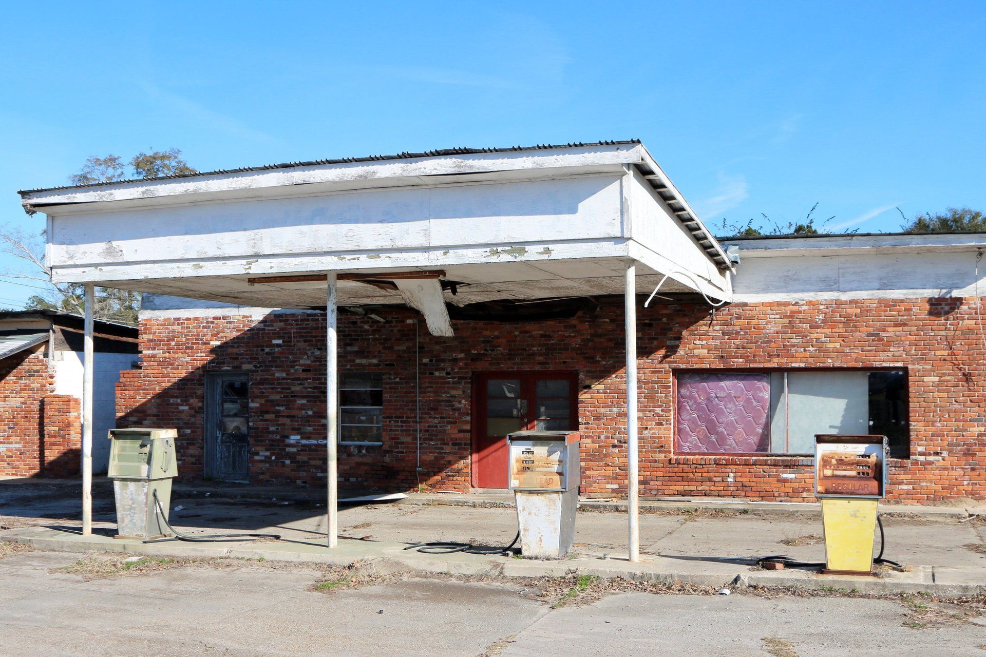 Abandoned brick gas station with faded canopy and weathered pumps.
