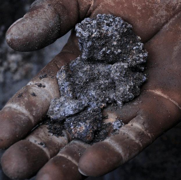 A handful of dark, textured mineral held in a dirt-stained palm.