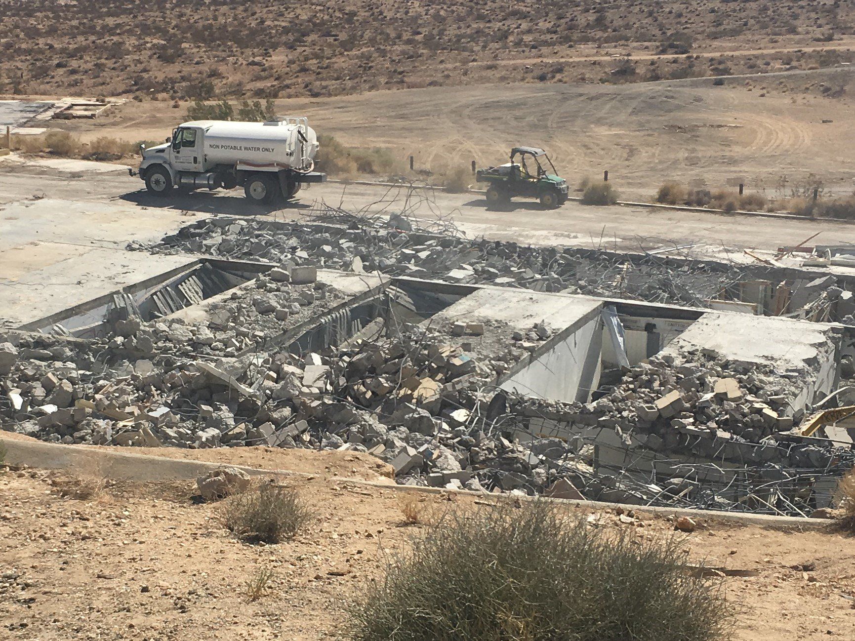 A white truck is driving down a dirt road next to a pile of rubble.
