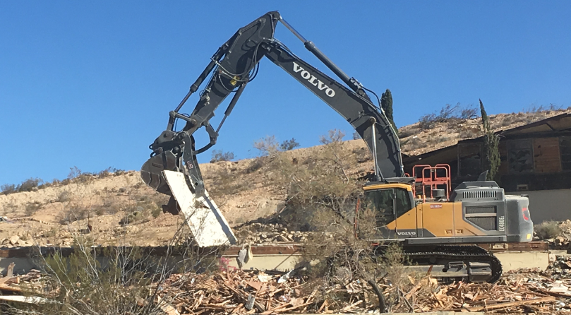 A volvo excavator is demolishing a building in the desert.