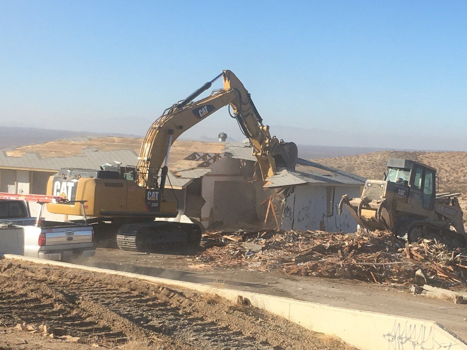 A cat excavator is demolishing a house in the desert.