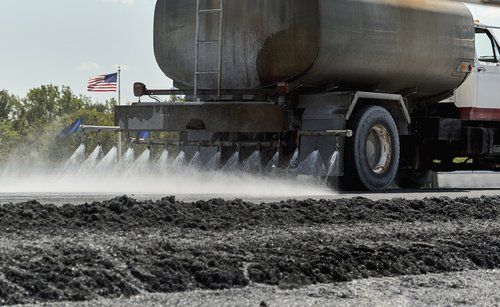 Truck spraying water on dirt road with an American flag in the background.