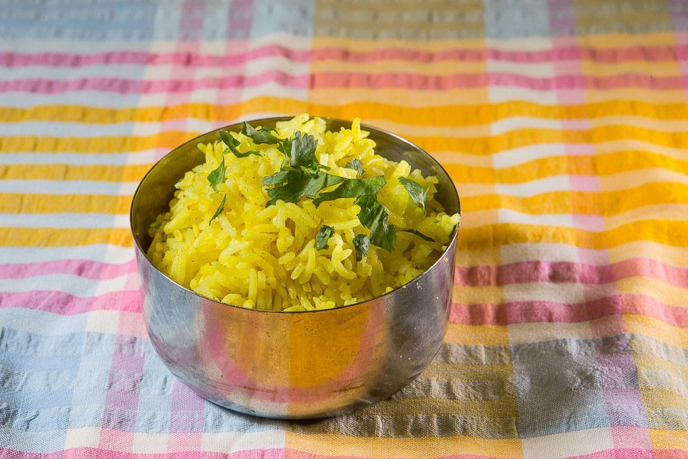 Bowl of yellow rice garnished with herbs on a colorful striped cloth