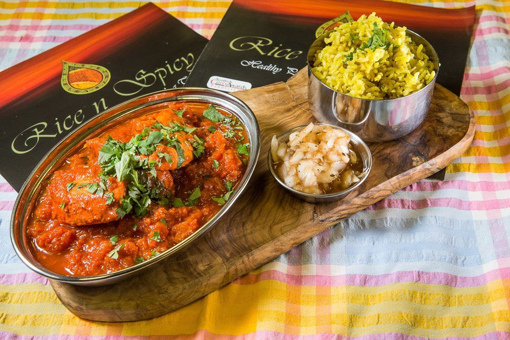 Two Indian curry dishes with rice and chutney on a wooden tray, served on a checkered cloth.