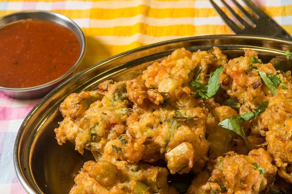 Spicy fried chicken in a metal bowl with red dipping sauce and green garnish on a striped tablecloth