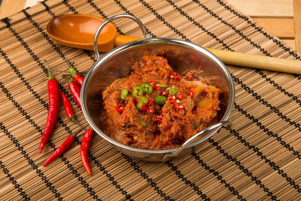 Spicy red chili paste in a bowl with red chilies and a wooden spoon on a woven mat