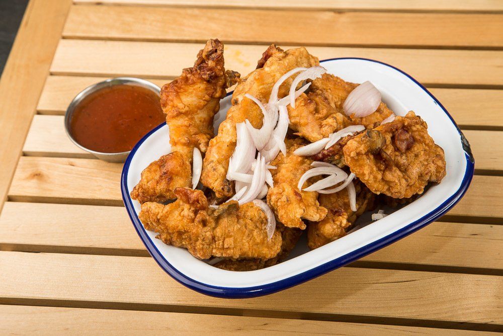 Fried chicken with onions and dipping sauce on a white plate with blue rim on a wooden table