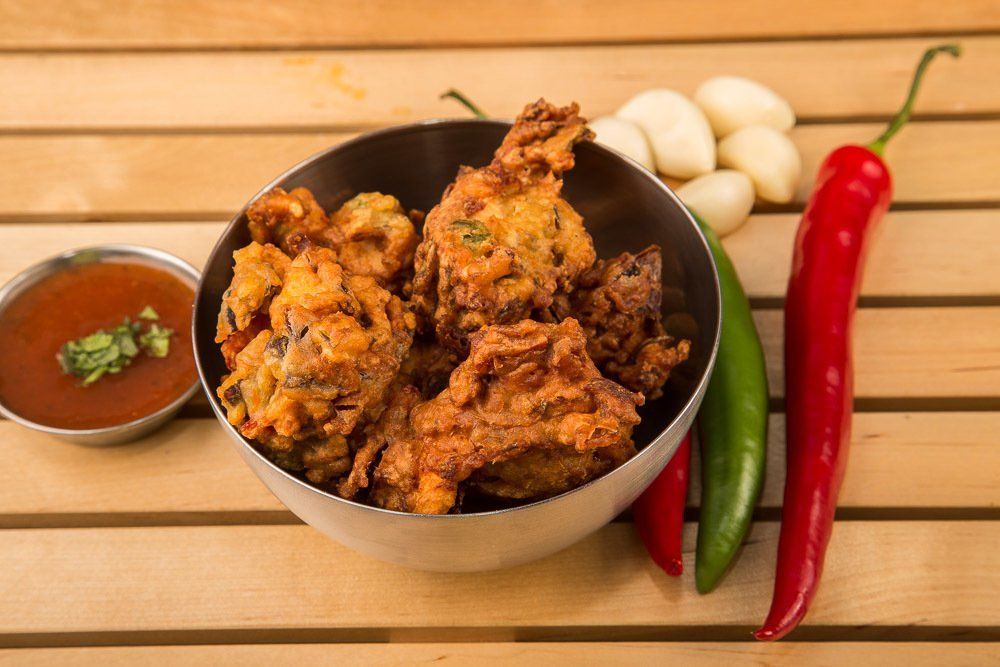 Spicy fried chicken in a bowl with chili peppers, eggs, and dipping sauce on a wooden table