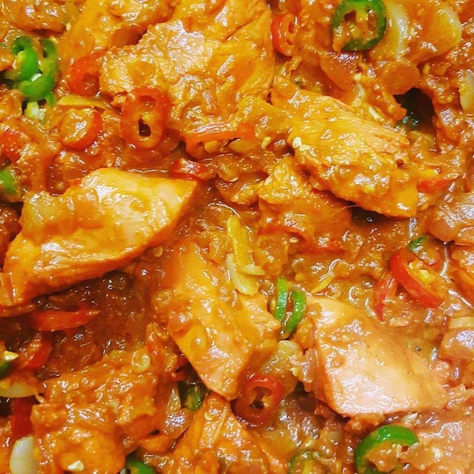 Close-up of spicy orange curry with chicken pieces and green chili slices