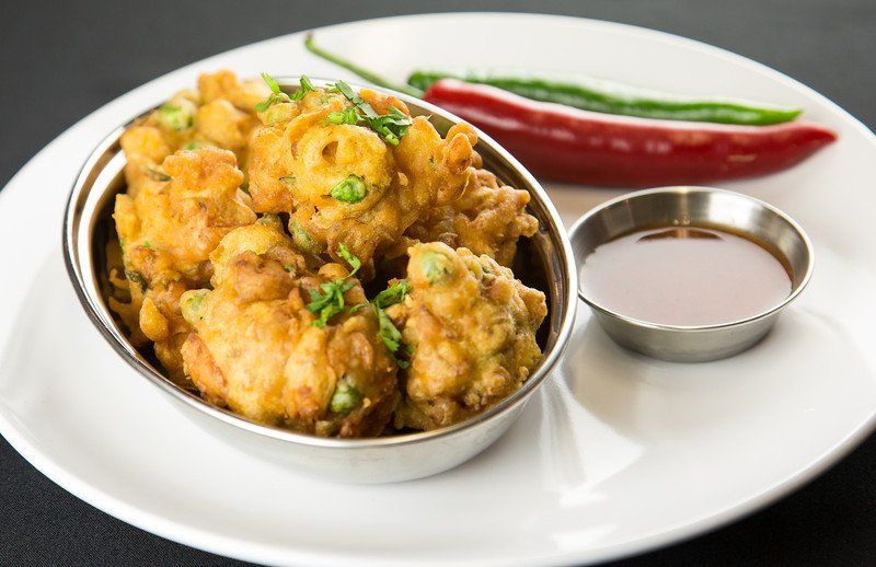 Spicy fried chicken in a bowl with dipping sauce and red chilies on a white plate