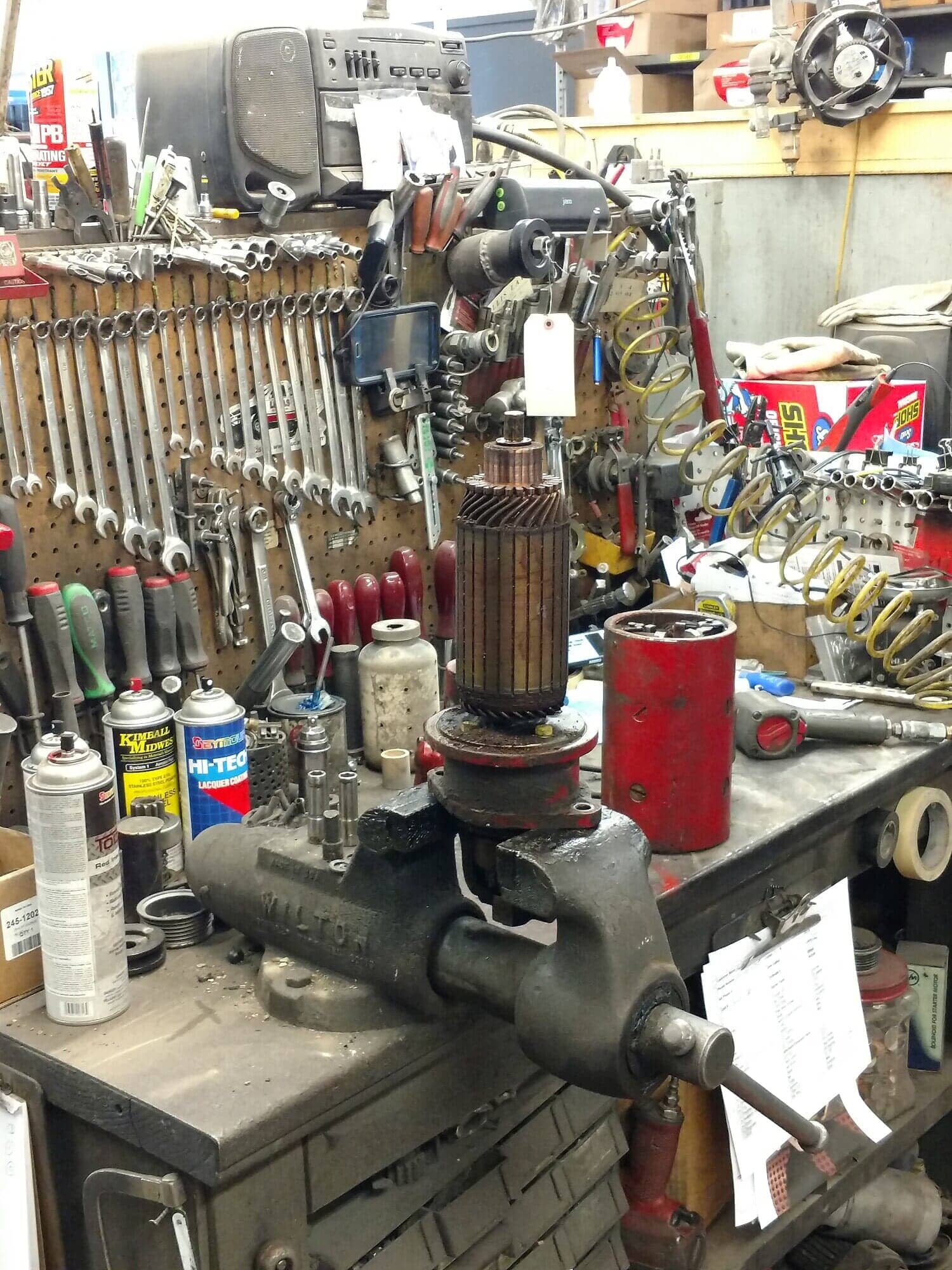 Engine block on a workbench in a cluttered auto repair shop, with tools and parts in the background.