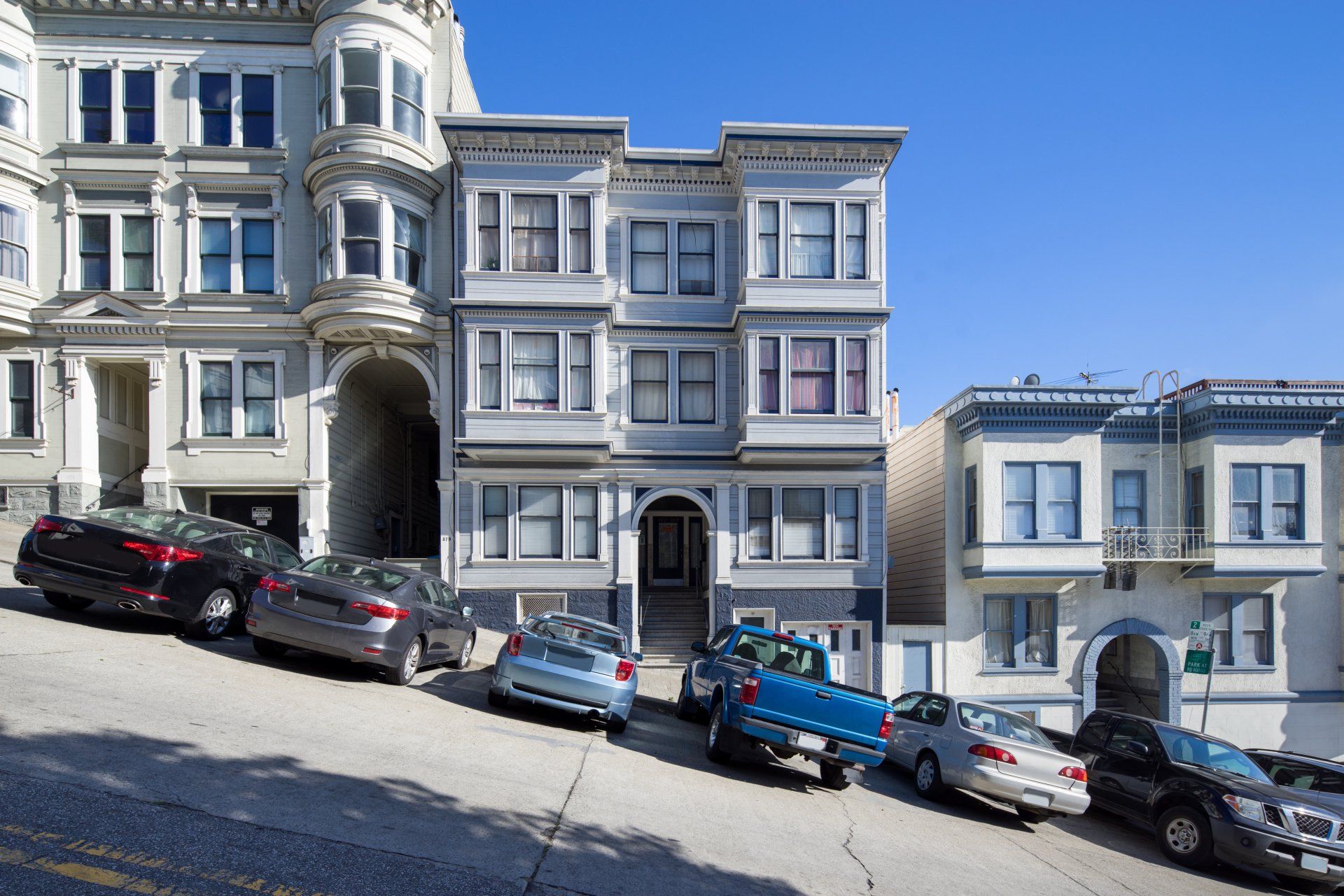 A row of cars are parked on a hill in front of a building